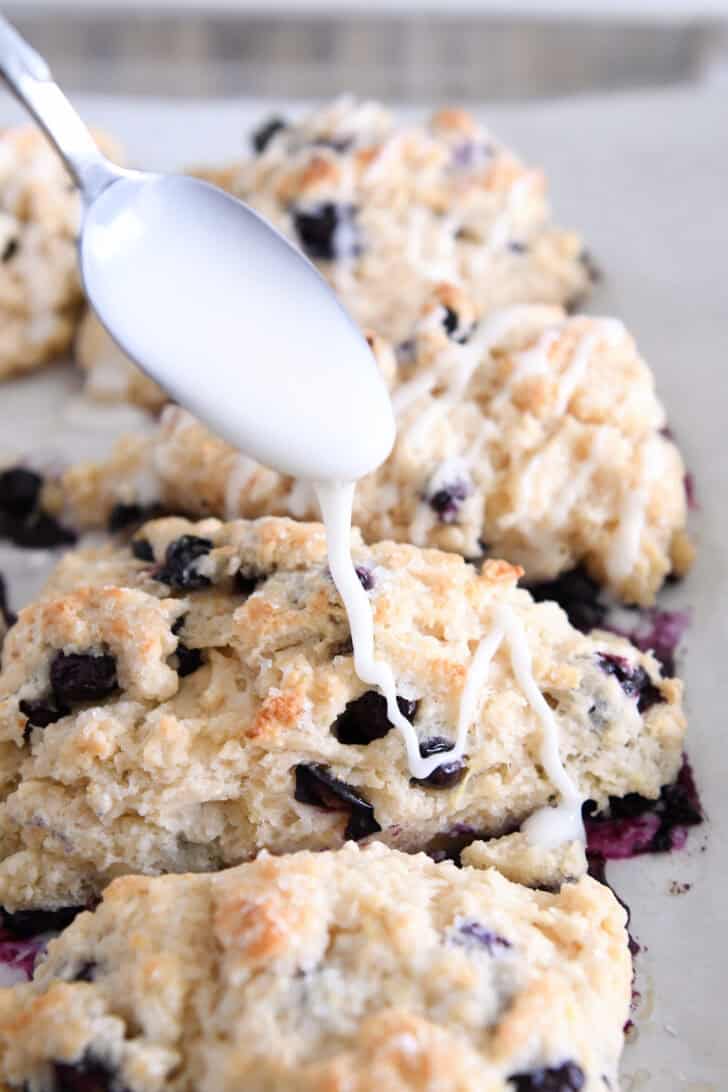Drizzling lemon glaze over baked lemon blueberry scones.