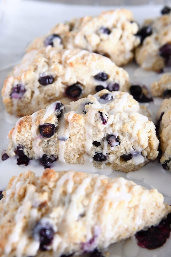 Glazed baked lemon blueberry scones on parchment lined baking sheet.
