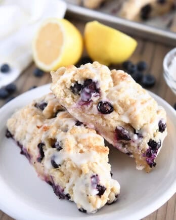 Two triangle-shaped baked lemon blueberry scones on white plate.