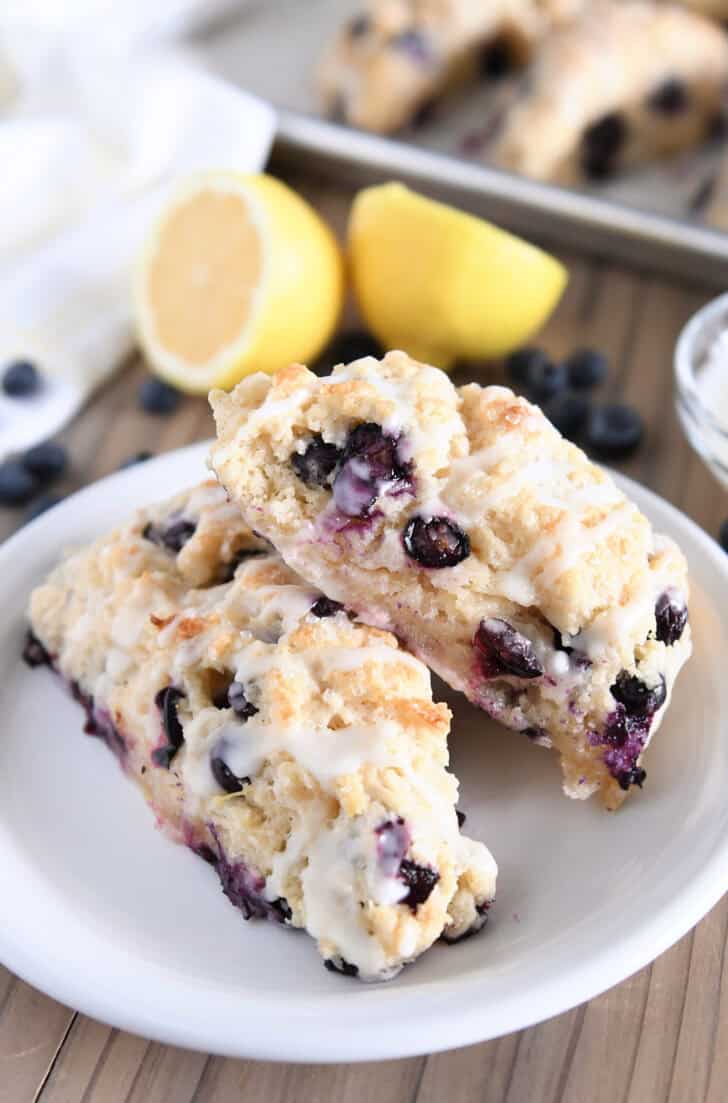 Two triangle-shaped baked lemon blueberry scones on white plate.