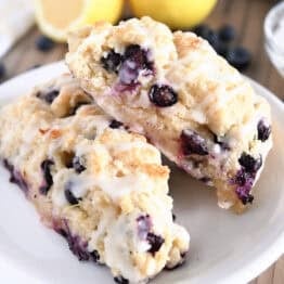 Two baked and glazed lemon blueberry scones on white plate.