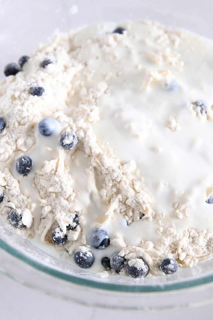 Buttermilk and lemon juice added to scone dough with blueberries in glass bowl.