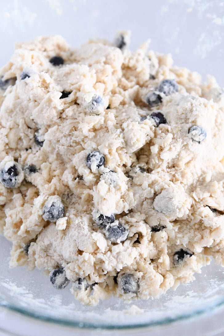 Crumbly scone dough with blueberries in glass bowl.
