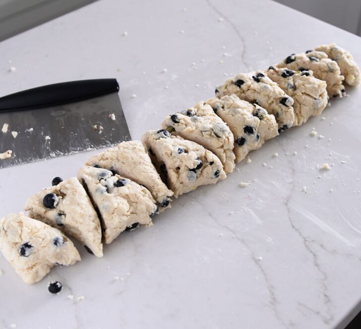 Scone dough cut into triangle pieces with bench scraper.