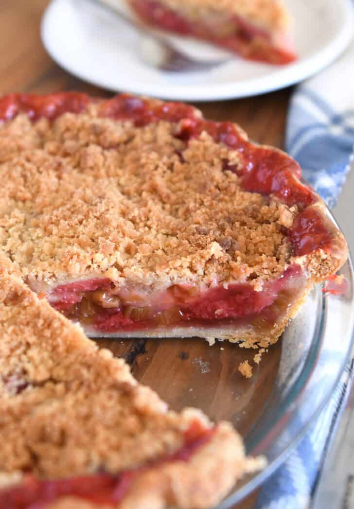 Strawberry rhubarb pie in glass pie plate with slice taken out.