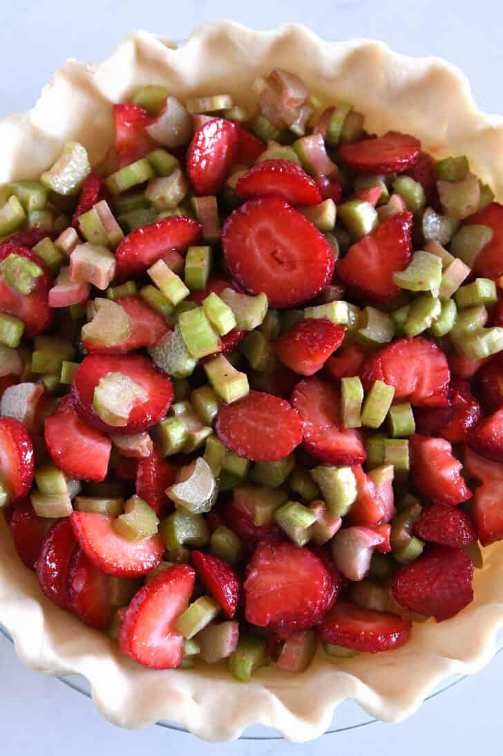 Pie crust in pie plate filled with unbaked strawberries and rhubarb.