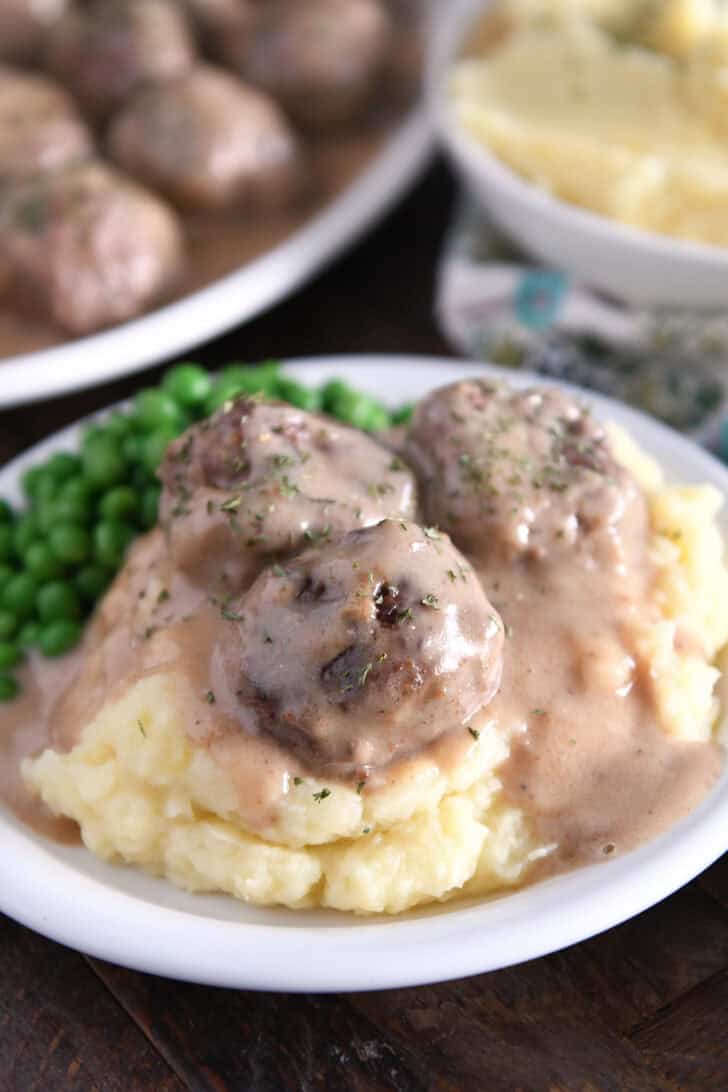 Three meatballs on top of pile of mashed potatoes smothered in thick brown gravy.