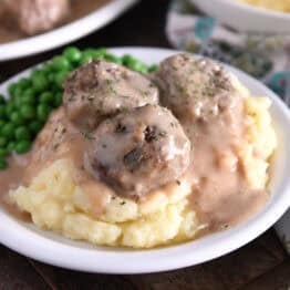 Three meatballs on top of pile of mashed potatoes smothered in thick brown gravy.