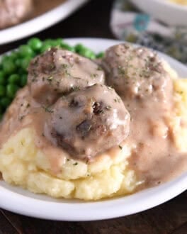Three meatballs on top of pile of mashed potatoes smothered in thick brown gravy.
