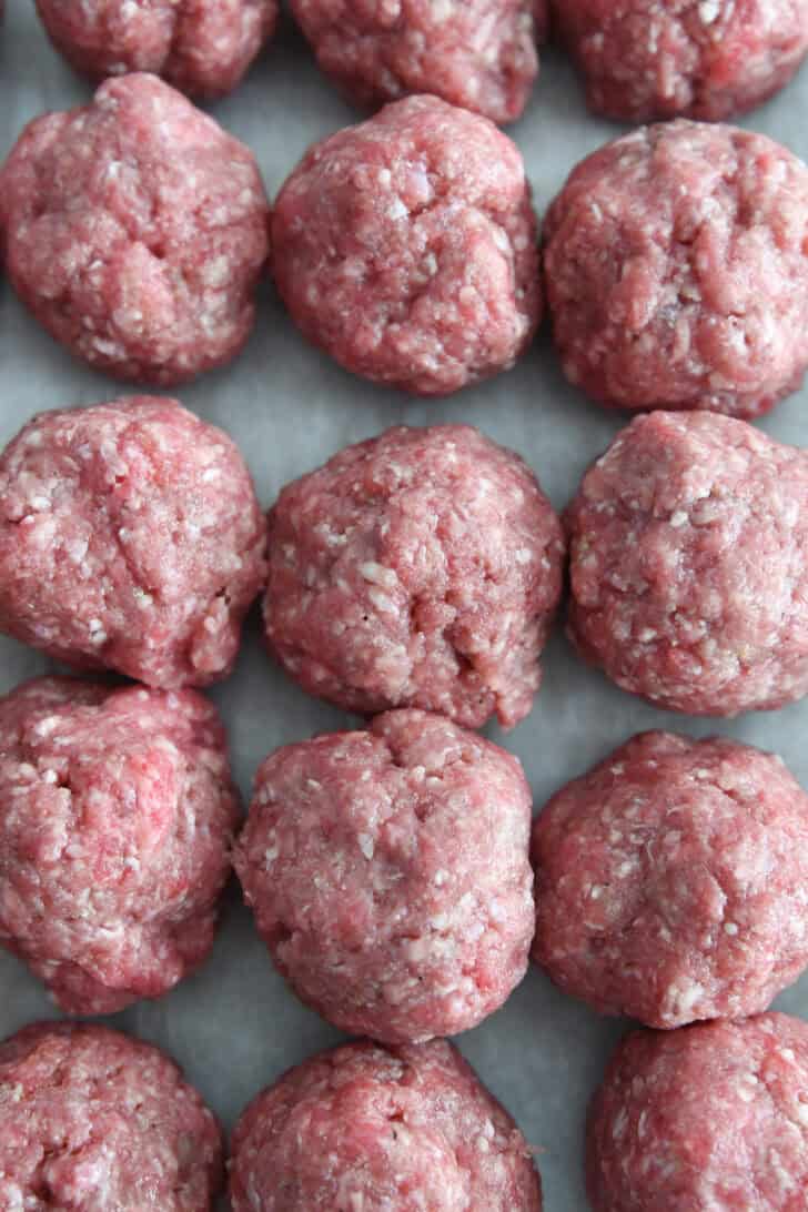 Top down view of nine unbaked meatballs on parchment paper.