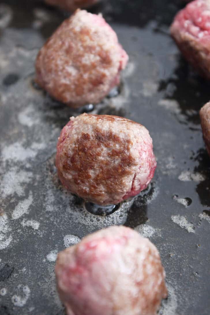 Partly browned meatballs in electric skillet in butter and olive oil.