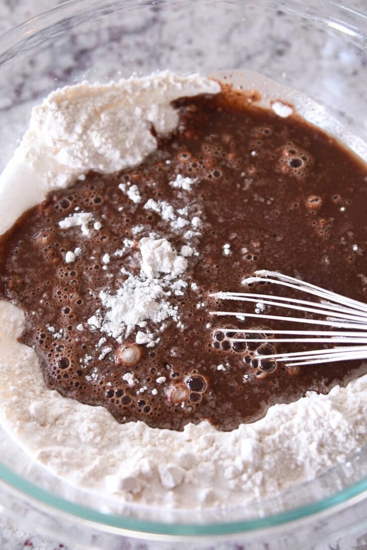 Top down view of a whisk in a glass bowl with flour and chocolate cake batter.