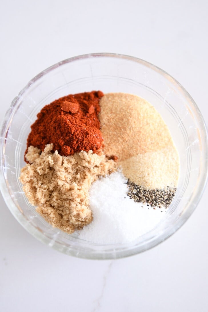 Smoked paprika, garlic powder, onion powder, brown sugar, salt and pepper in glass bowl.