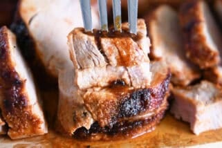 Fork piercing two stacked pieces of cooked pork tenderloin on wood cutting board.