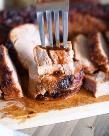 Fork piercing two stacked pieces of cooked pork tenderloin on wood cutting board.