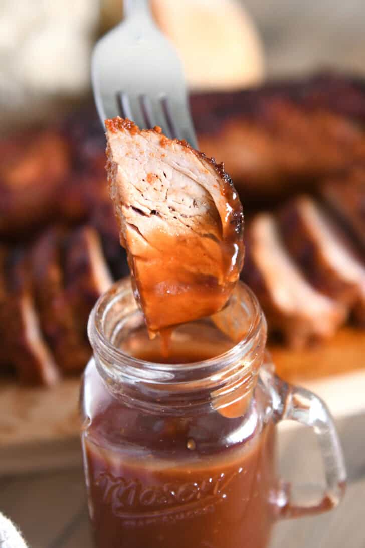 Fork spearing piece of cooked pork tenderloin dipped in BBQ sauce.