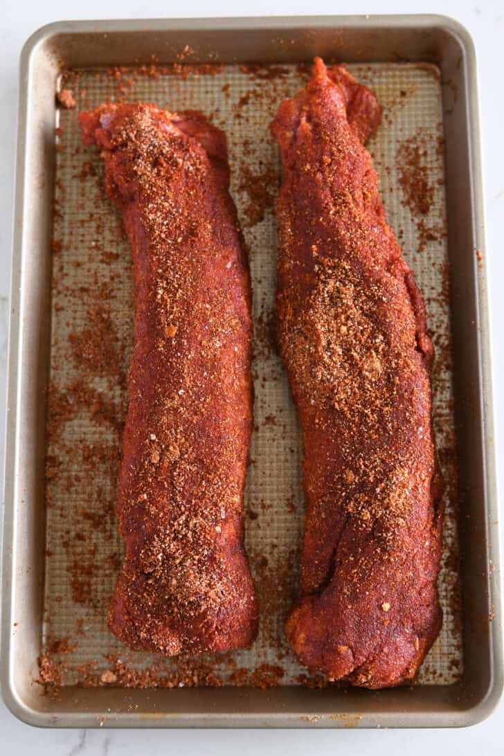 Top down view of two spice-crusted pork tenderloins on gold baking sheet.