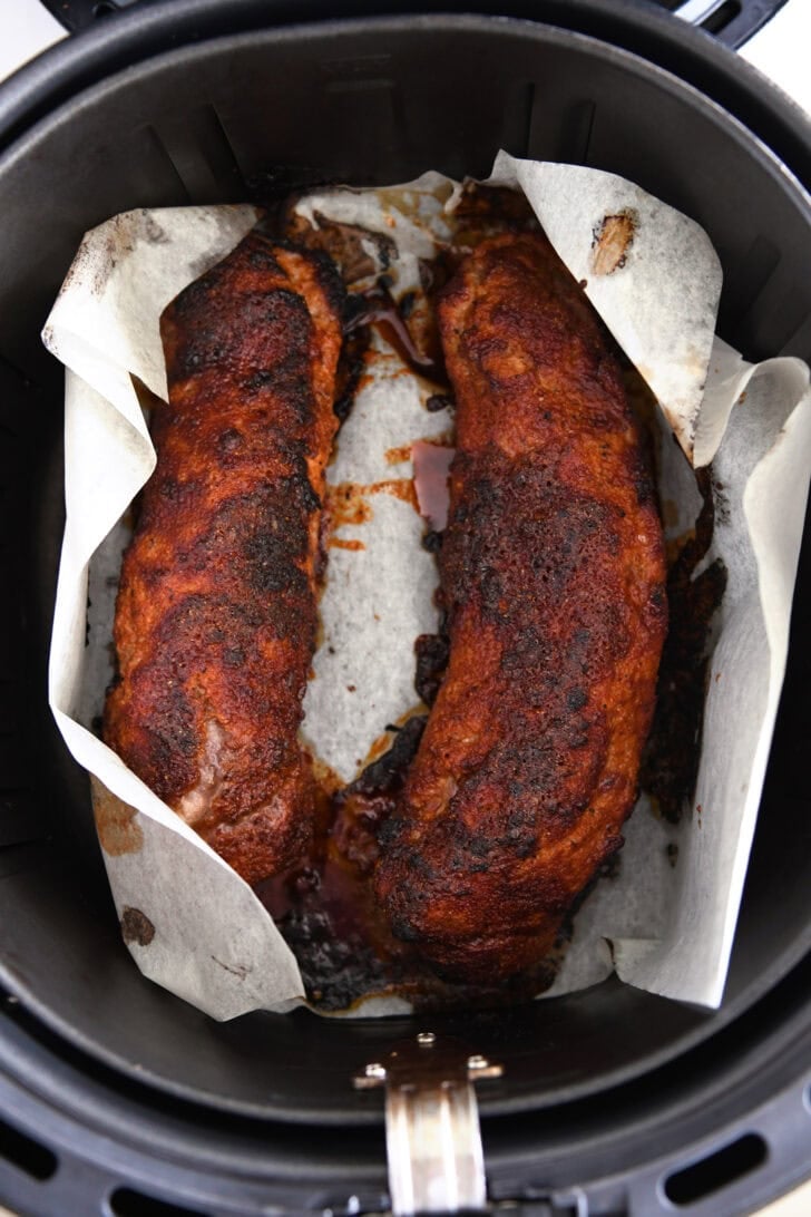 Two pork tenderloins in air fryer on parchment paper.