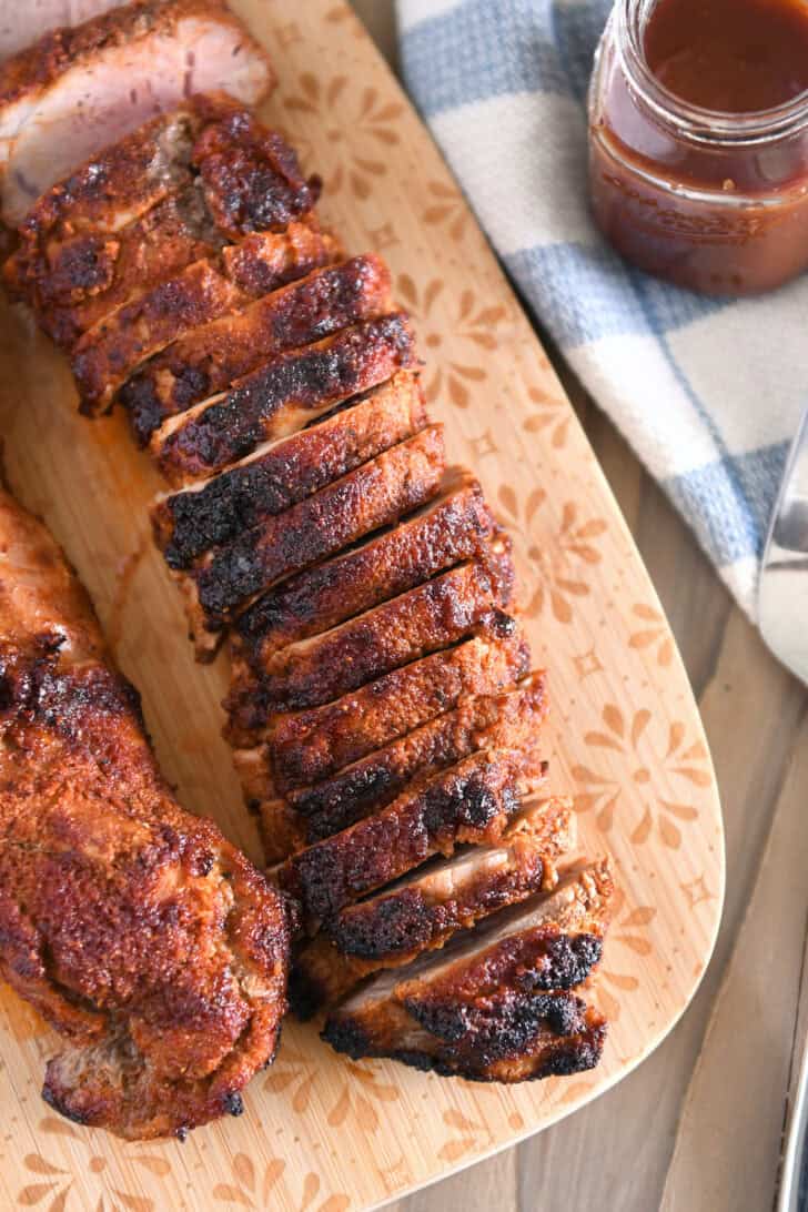 Top down view of sliced pork tenderloin on wood cutting board.