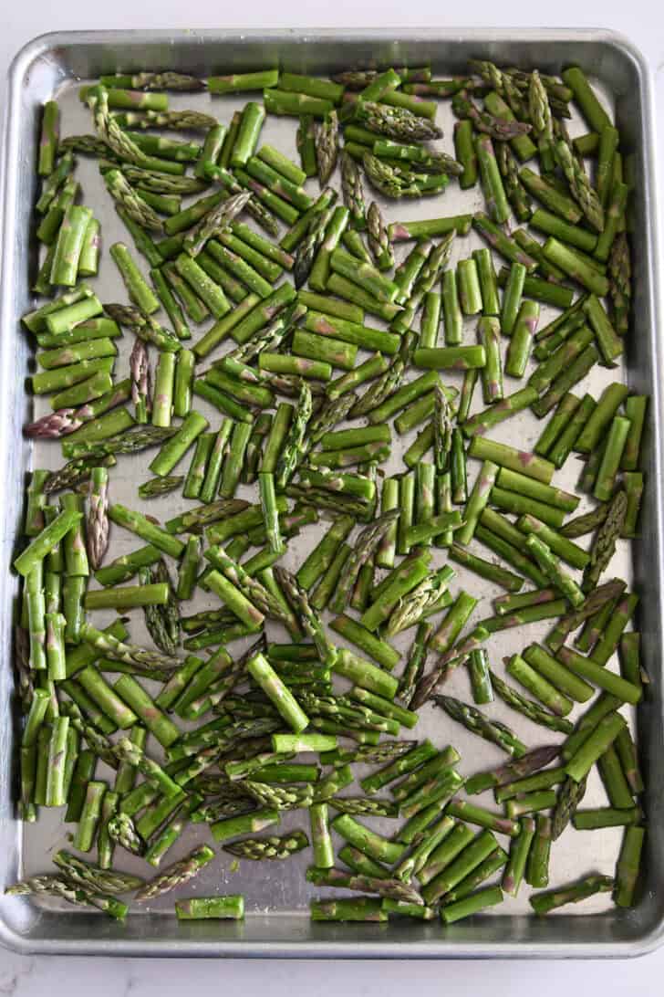 Asparagus pieces on sheet pan with olive oil and salt.