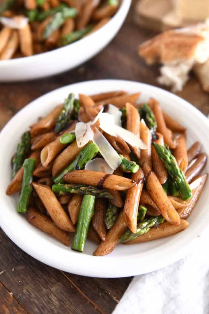 White plate with balsamic drenched penne pasta, roasted asparagus and parmesan cheese.