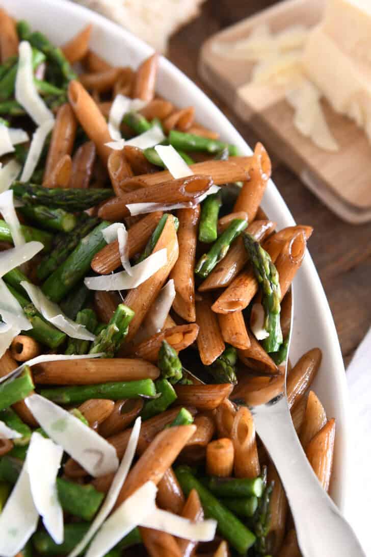 Serving spoon in dish with balsamic penne pasta, roasted asparagus and parmesan cheese.