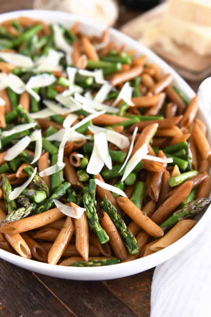White serving dish with balsamic penne pasta, roasted asparagus and parmesan cheese.