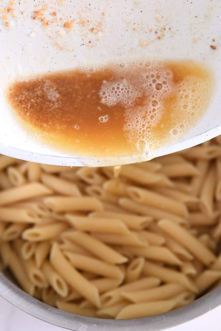 Pouring brown butter over penne pasta.