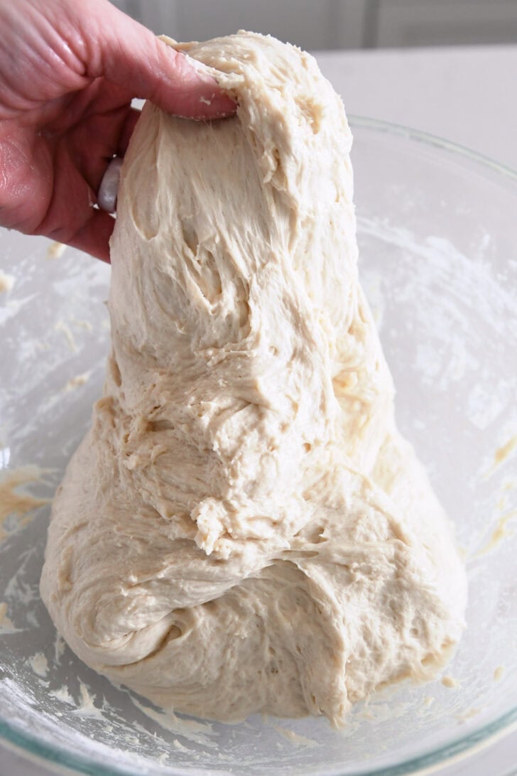 Lifting dough up for stretch and folds in a glass bowl.