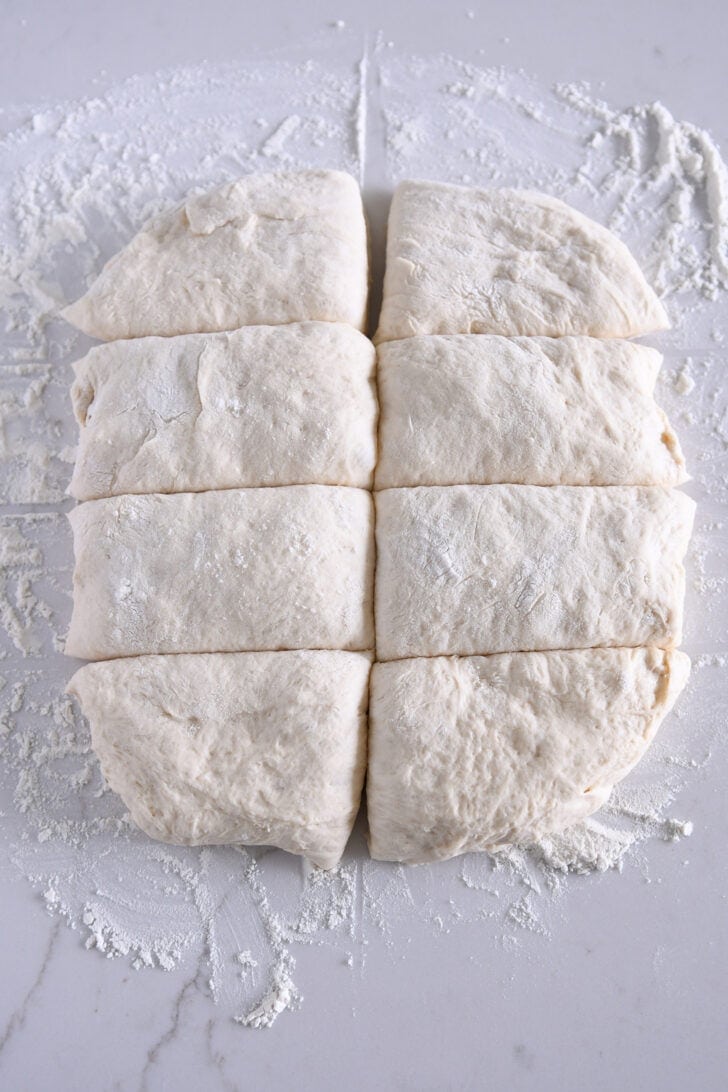 Soft ciabatta dough cut into eight pieces.