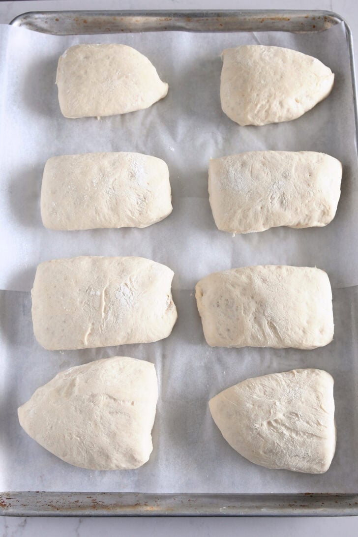 Eight ciabatta rolls rising on sheet pan.
