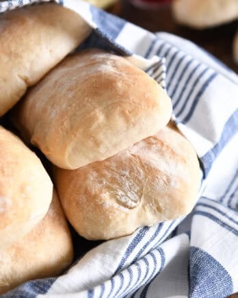 Several baked ciabatta rolls with blue and white towel in white dish.