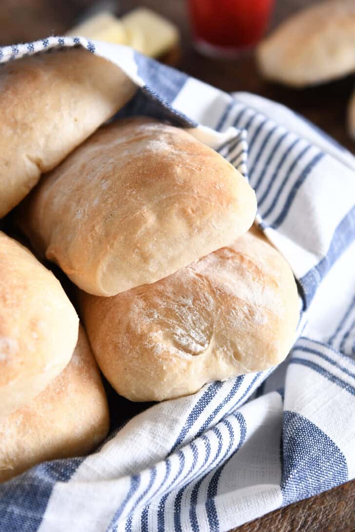 Several baked ciabatta rolls with blue and white towel in white dish.