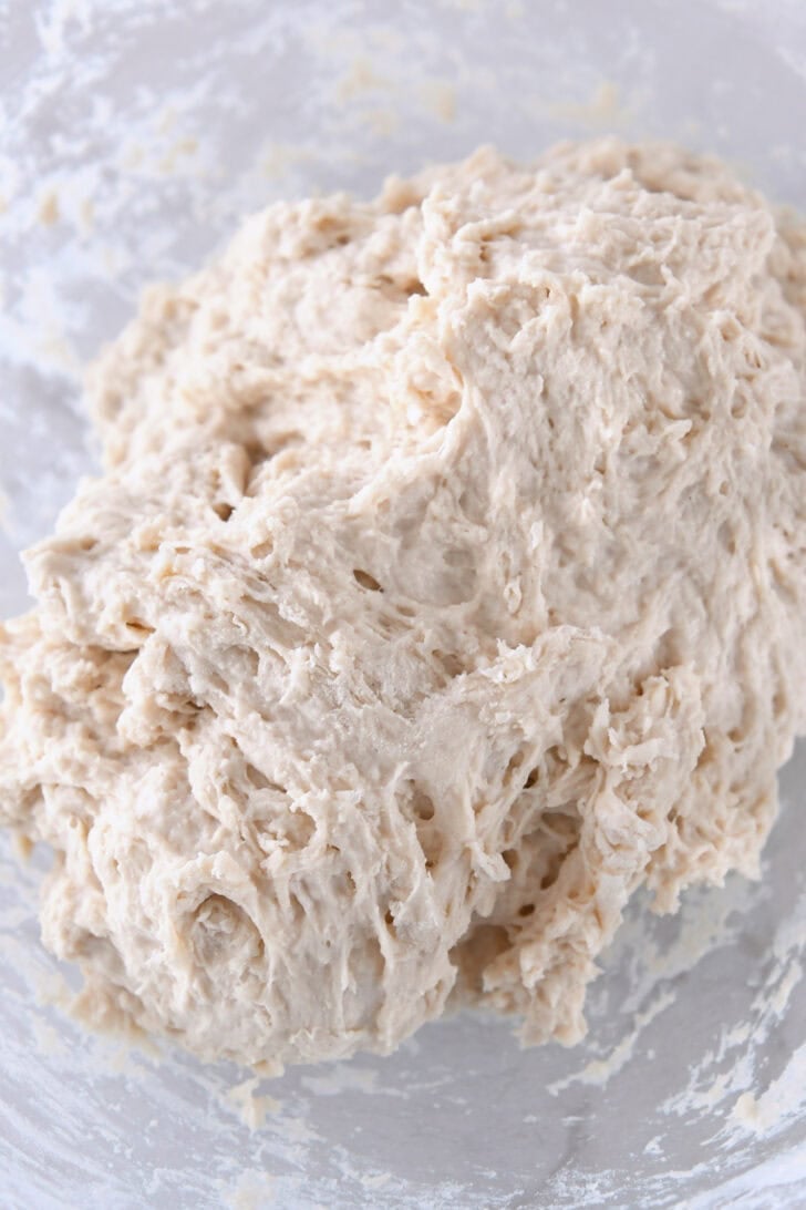 Glass bowl with shaggy-looking ciabatta roll dough.