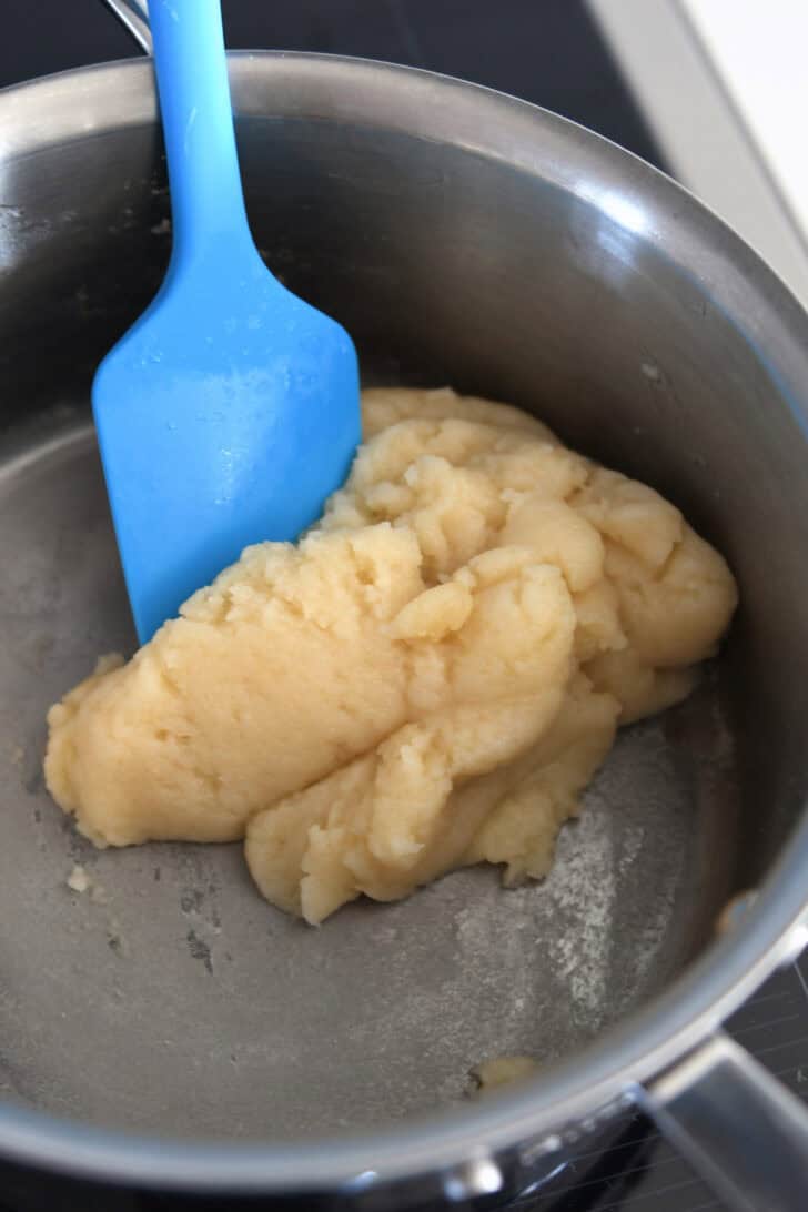 Cream puff mixture stirred into a ball in saucepan.