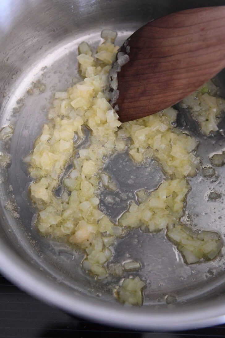 Sautéing garlic and onions in olive oil in stainless pot with wooden spoon.