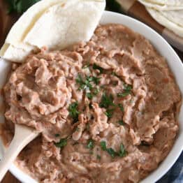 Top down view of white bowl with easy refried beans, cilantro and tortillas.