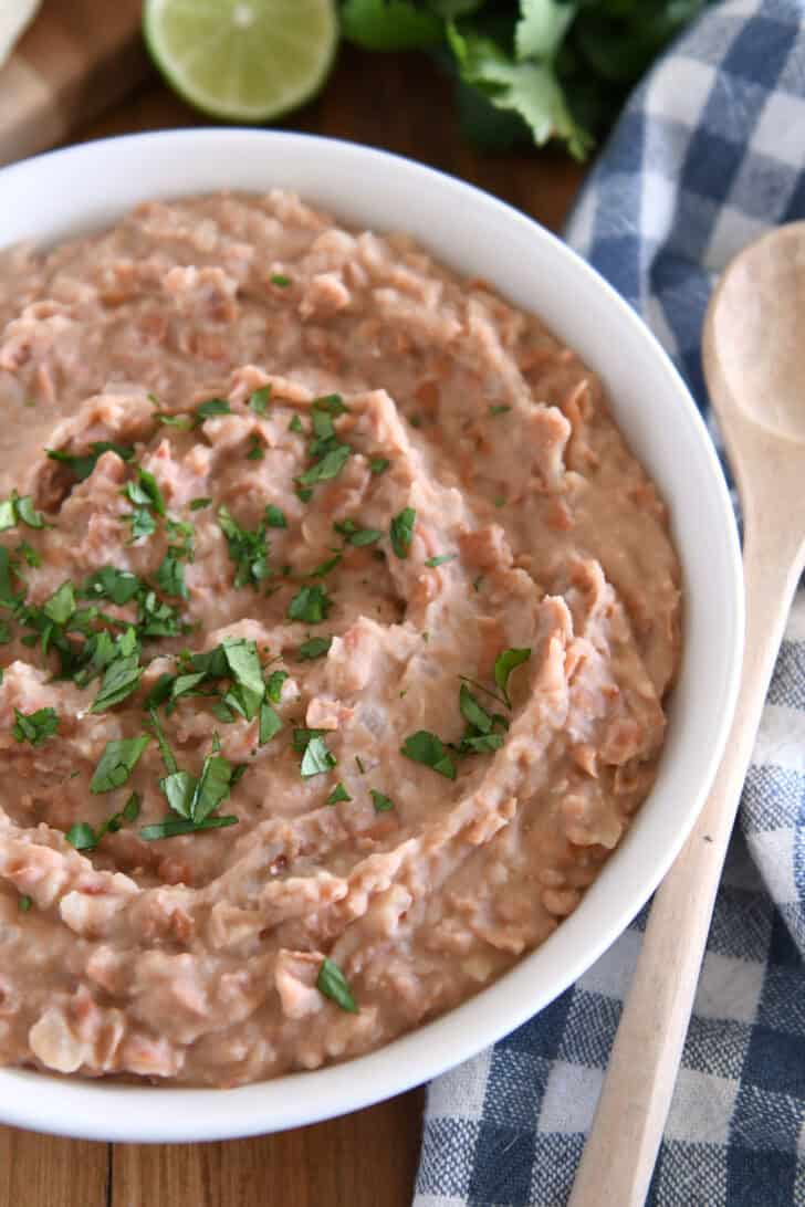 Easy creamy refried beans in white bowl with fresh cilantro.