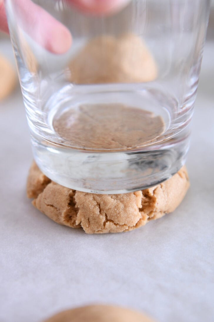 Pressing peanut butter cookie flat with glass.