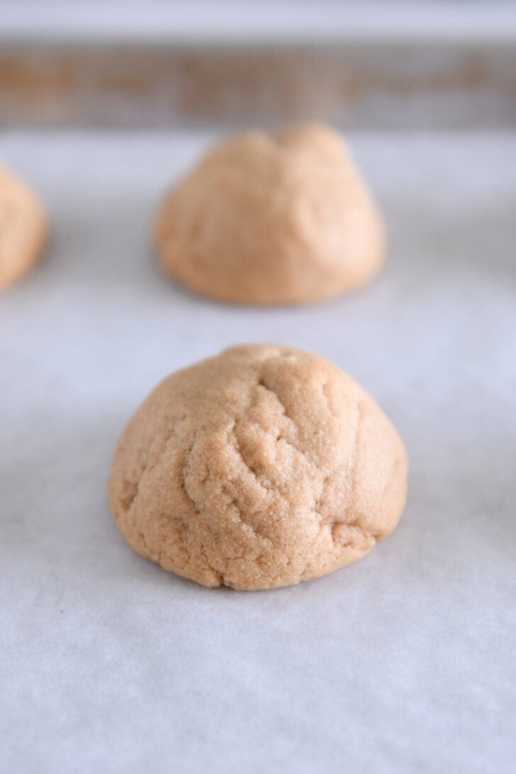 Baked puffy peanut butter cookie on white parchment paper.