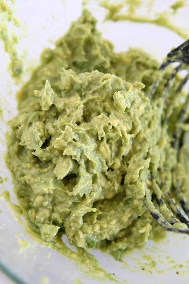 Mashed avocado guacamole in glass bowl.