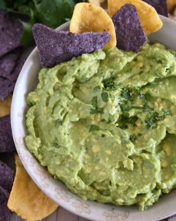 Top down view of homemade guacamole in tan bowl with chopped cilantro and tortilla chips.