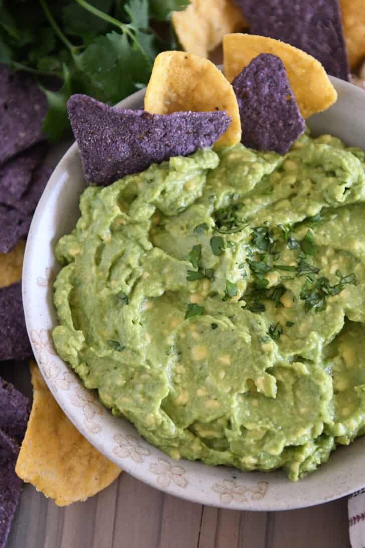 Top down view of homemade guacamole in tan bowl with chopped cilantro and tortilla chips.
