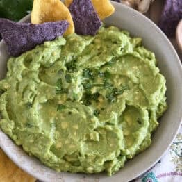 Top down view of homemade guacamole in tan bowl with chopped cilantro and tortilla chips.