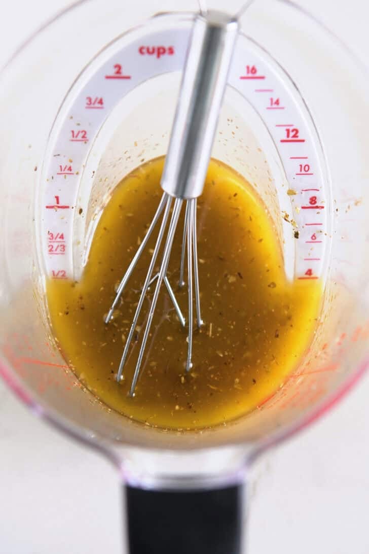 Liquid measuring cup with olive oil, lemon juice, oregano and garlic.