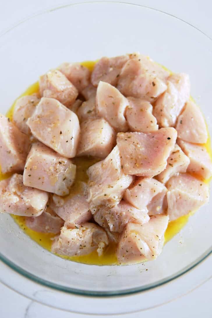 Glass bowl with chicken pieces marinating in lemon juice, olive oil and oregano.