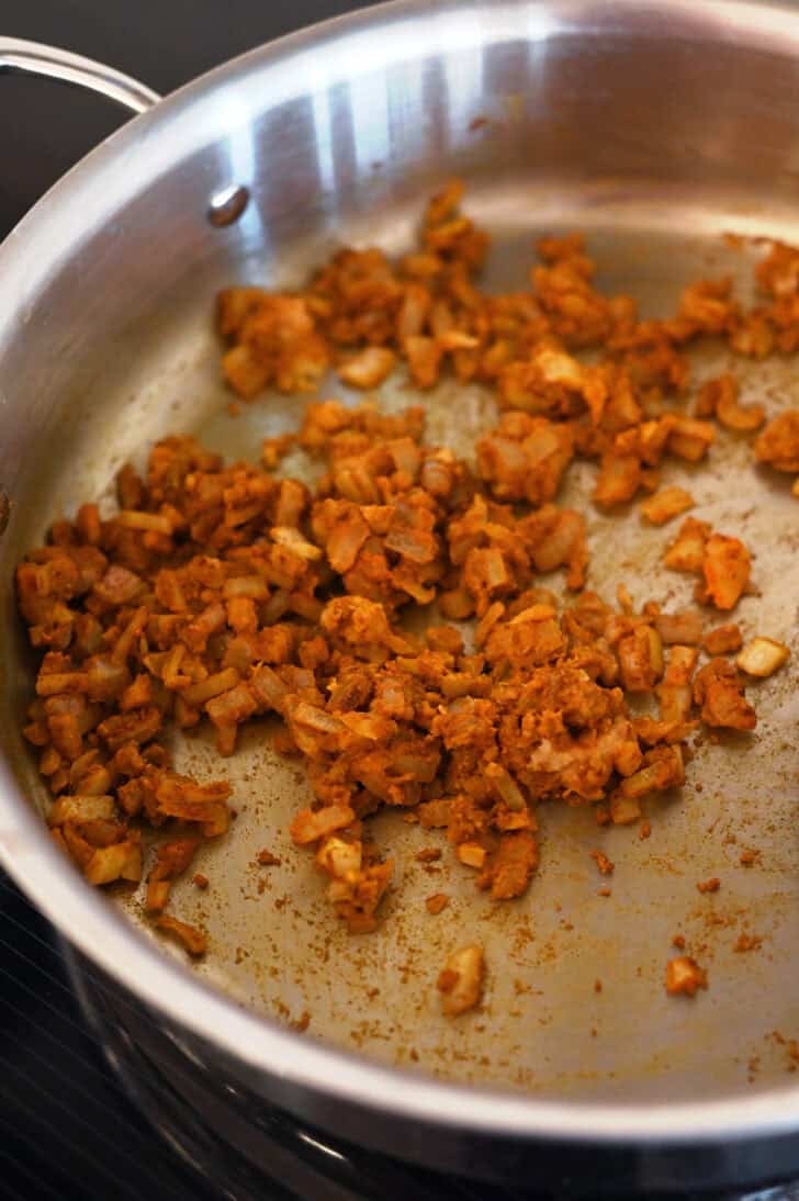 Curry spices and onions cooking in a metal pot.