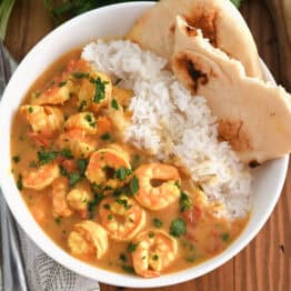 Top down view of a white bowl with flatbread, white rice, and shrimp in a curry sauce.