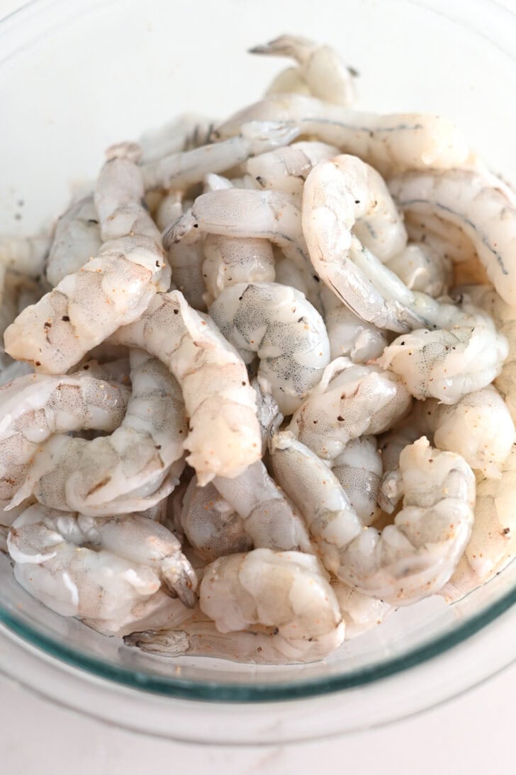 Top down view or raw shrimp in a glass bowl.
