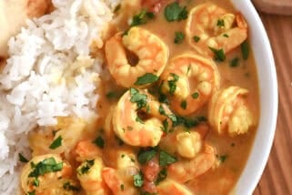 Top down view of a white bowl with flatbread, white rice, and shrimp in a curry sauce.